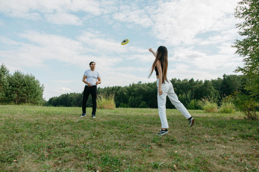 Man and woman playing frisbee outdoors, enjoying light movement and fresh air to counteract the effects of prolonged sitting