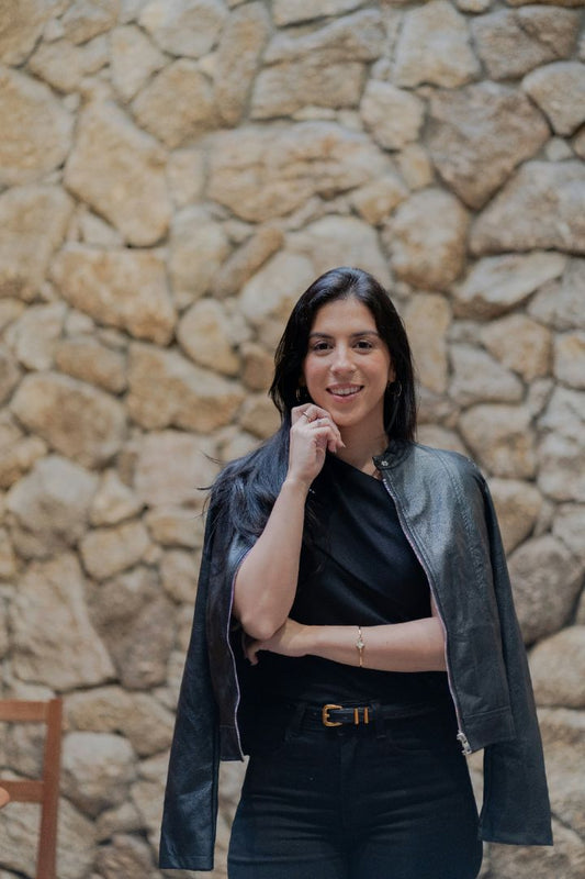 Confident woman with dark features smiling in front of a blurred stone wall, representing clarity, strength, and improved focus from simple science-backed changes