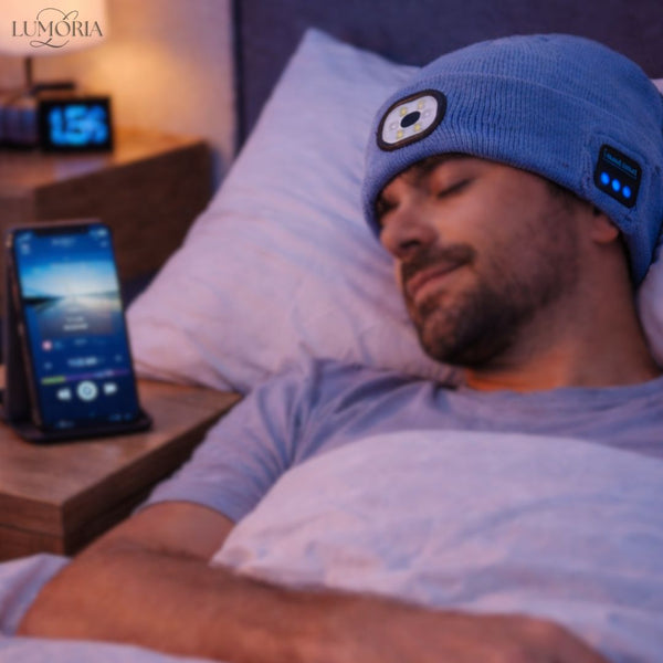 Man sleeping while wearing the GlowSound Beanie™ with Bluetooth audio and built-in LED light, hands-free music playing from a smartphone beside the bed