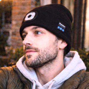 Person wearing a black beanie with Bluetooth speaker, blurred background