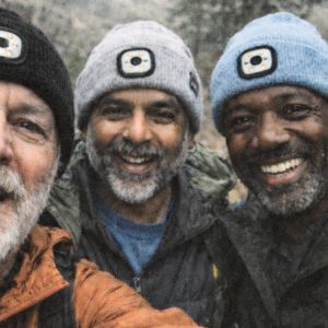 Three men wearing beanies with a light, smiling outdoors.